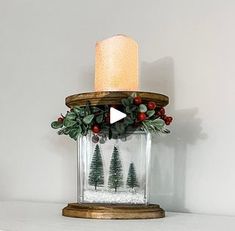 a candle that is sitting on top of a shelf with snow and evergreens in it