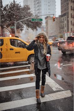 a woman walking across a street in the snow with a cup of coffee on her hand