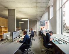 two men sitting at desks in an office with large windows and bikes on the wall