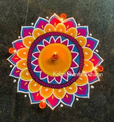 a colorful flower design with a lit candle on the ground in front of it,