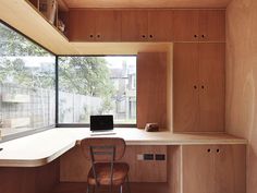 a desk with a laptop on top of it next to a window and wooden cabinets