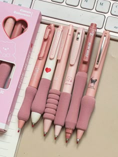 several pink pens are lined up next to a computer keyboard and pen holder with heart shaped erasers on it