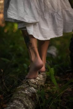 a woman with tattoos walking on a log in the woods