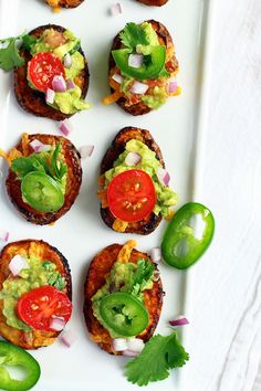 several small sandwiches with toppings on a white plate next to peppers and jalapenos