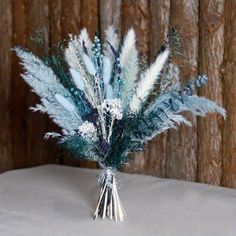 some blue and white feathers are in a vase on a table with wood wall behind it