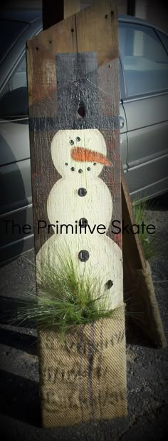 a wooden sign with a snowman painted on it's face and grass growing in the bottom