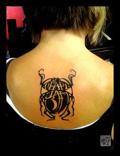 the back of a woman's neck with a black and white beetle tattoo on it