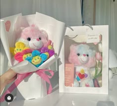 a pink teddy bear in a white box with other stuffed animals inside it, and an open gift bag on the table