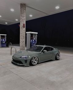 a grey sports car parked in front of a gas station at night with no one around