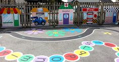 children's play area with painted letters and flowers on the pavement in front of a fence