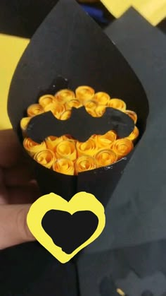 a hand holding a black box with yellow roses in the shape of a batman symbol