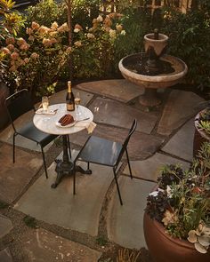 a small table with two chairs and a bottle of wine on it in the middle of a garden