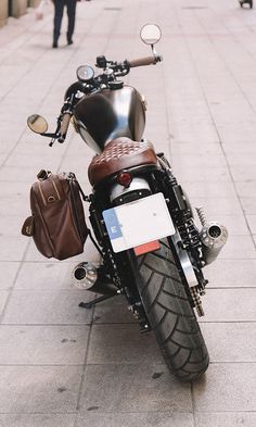 a black motorcycle parked on the side of a street next to a sidewalk with people walking by