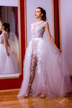 a woman standing in front of a mirror wearing a white dress with flowers on it