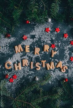 the word merry christmas spelled out in wooden letters surrounded by pine branches and ornaments on a dark background