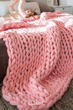 a woman laying on top of a bed under a pink blanket