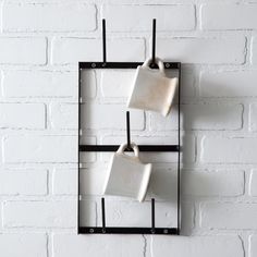 two mugs are hanging on the wall in front of a white brick wall with black metal frame