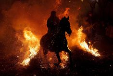 a man riding on the back of a horse in front of a fire filled sky