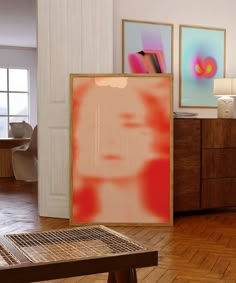 an abstract painting is on display in a room with wooden floors and white walls, along with two framed art pieces