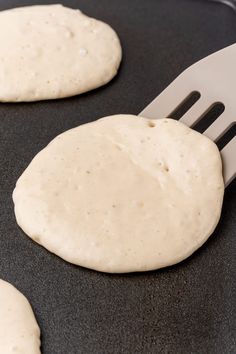 two uncooked pizza doughs on a pan with a spatula in the middle