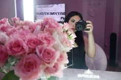 a woman taking a selfie in front of a mirror holding a camera and flowers