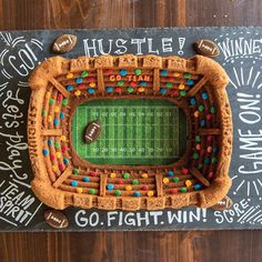 a cake shaped like a football stadium on top of a chalkboard with writing all over it