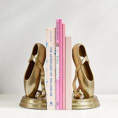 a pair of gold shoes sitting on top of a bookend next to two books