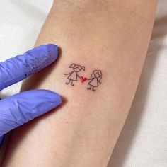 a woman's arm with a small tattoo on it that has two people holding a heart