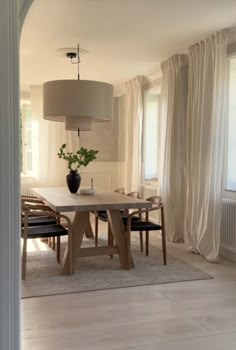 a dining room table with chairs and a vase on it in front of a window