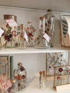 several glass bottles with flowers in them on a shelf next to other items and papers