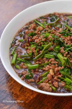 a white bowl filled with meat and veggies on top of a wooden table