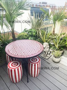 an outdoor table and two stools on a deck with potted plants in the background