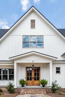 a white house with two large windows on the front and side of it, surrounded by greenery