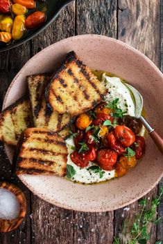 a bowl filled with grilled bread, tomatoes and sour cream on top of a wooden table