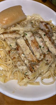 a white plate topped with pasta and meat covered in gravy on top of a wooden table