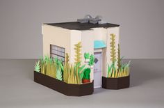 a paper model of a house with grass and plants on the front, and an open door in the back