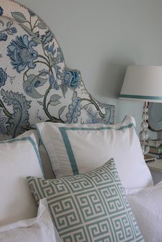 a bed with blue and white pillows on top of it next to a night stand