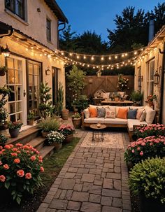 an outdoor patio with lights strung over it and flowers in the foreground, along with potted plants on either side