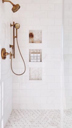 a bathroom with white tile and gold fixtures on the shower head, wall lights, and tiled floor