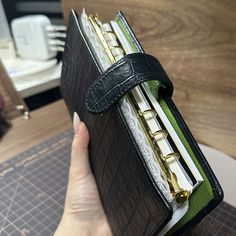 a hand holding a black leather binder on top of a wooden table next to a computer keyboard