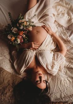 a pregnant woman laying on top of a bed next to a flower bouquet in her belly