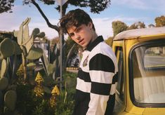 a young man standing next to a yellow truck in front of a cactus tree and shrubbery