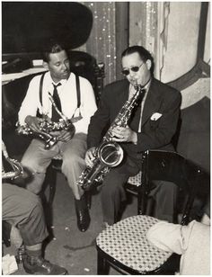 three men in suits and ties are playing saxophones while one man sits on a chair