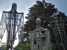 three halloween decorations in the shape of skeletons and ghost heads, with trees in the background