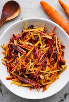 a white bowl filled with carrots and cranberry slaw next to two wooden spoons