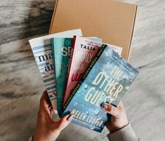 a person holding five books in front of a box on a marble counter top with the title, the other guide