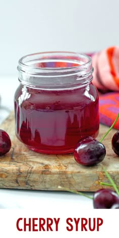 a jar of cherry syrup sitting on top of a cutting board next to some cherries