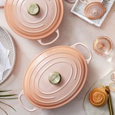 two pink pots sitting on top of a table next to glasses and utensils