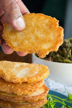 a person is picking up some fried food from a blue plate with greens in the background