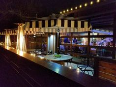 an outdoor dining area at night with lights on the tables and awnings over it